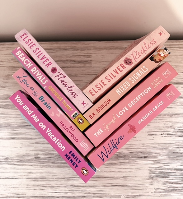 eight pink book spines arranged in a chevron pattern on a wood table.
