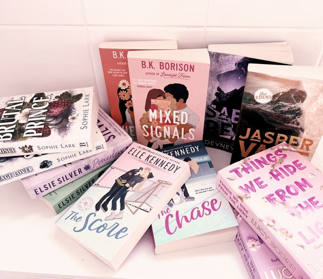 eleven books on a white counter. Some of the books include "The Score" by Elle Kennedy and "Mixed Signals" by B.K Borison.