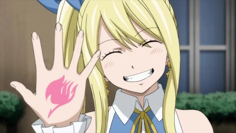 Lucy Heartfilia grinning while showing her Fairy Tail mark on the back of her right hand