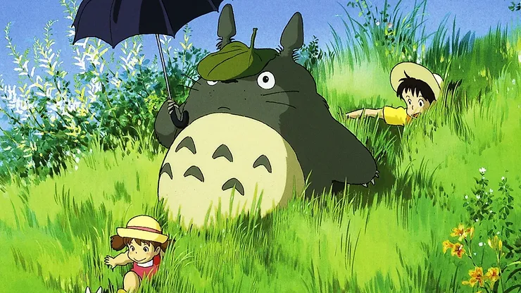 Mei, Satsuki, and Totoro all playing in a bright meadow with Totoro carrying a black umbrella.