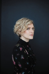 Heather O'Neill wears a black floral blouse and stands in front of a dark blue background.