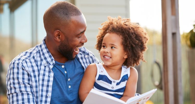 A man reading to a young girl outside.