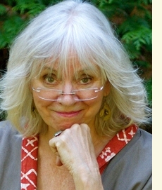 A gray-haired woman peers over her glasses with a smile.
