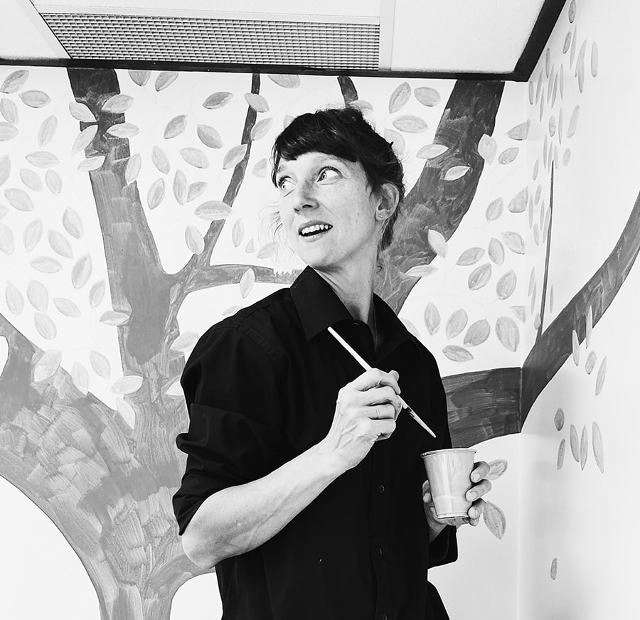 A woman looks over her shoulder with a paint brush in hand.