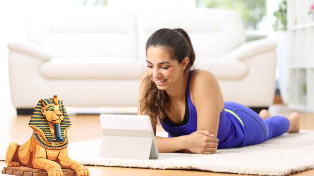 A lady viewing a tablet is lying on her stomach, propping herself up with her forearms. A small sphinx faces her in the bottom left side.