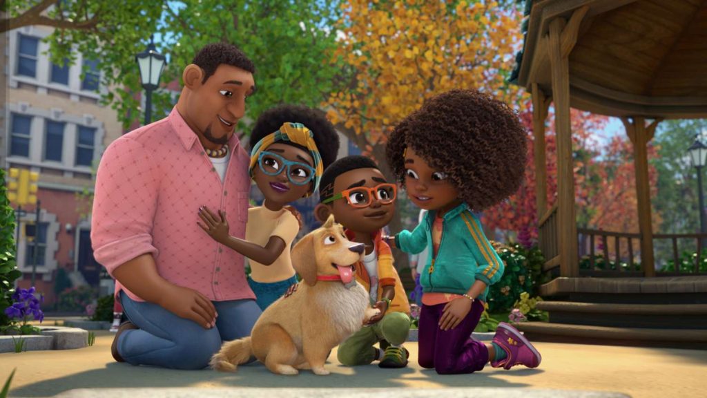 Screenshot of Karma's World, featuring a brown-skinned, curly-haired family of two adults and two children as well as a yellow medium-sized dog, all kneeling on the ground in a park and smiling at one another.