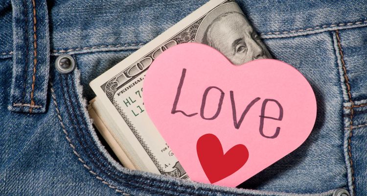 A pink heart-shaped note with the word 'Love' and a red heart symbol peeking out of a denim pocket, alongside U.S. dollar bills. Symbolizing the costs of Valentine's Day.