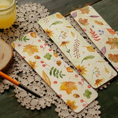 Fall-themed painted bookmarks on a wooden table with a doily underneath them.