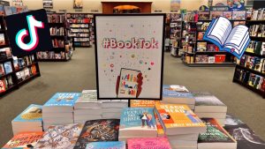 Display of books in a bookstore with a #BookTok sign. The TikTok logo appears on the left while a graphic of an open book is depicted on the left.