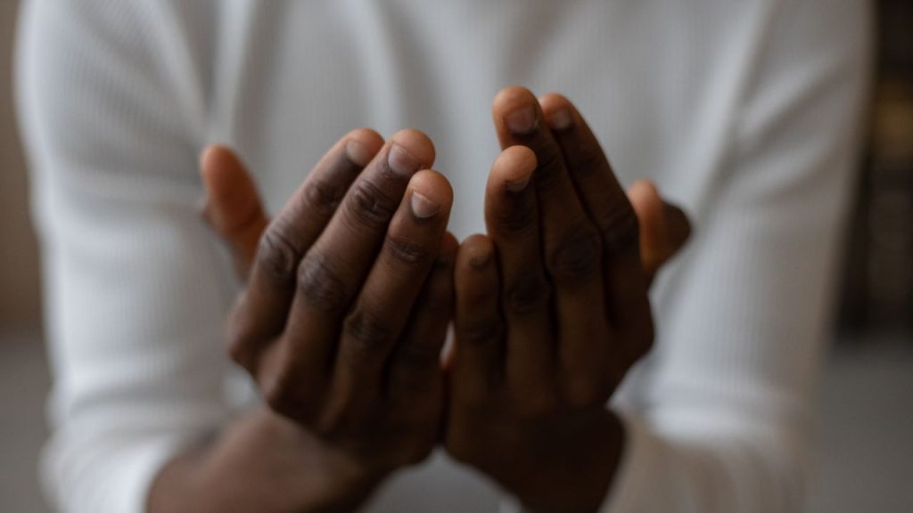 A man with his hand out almost as if he is praying. Nothing else is showing besides his white long sleeve shirt.