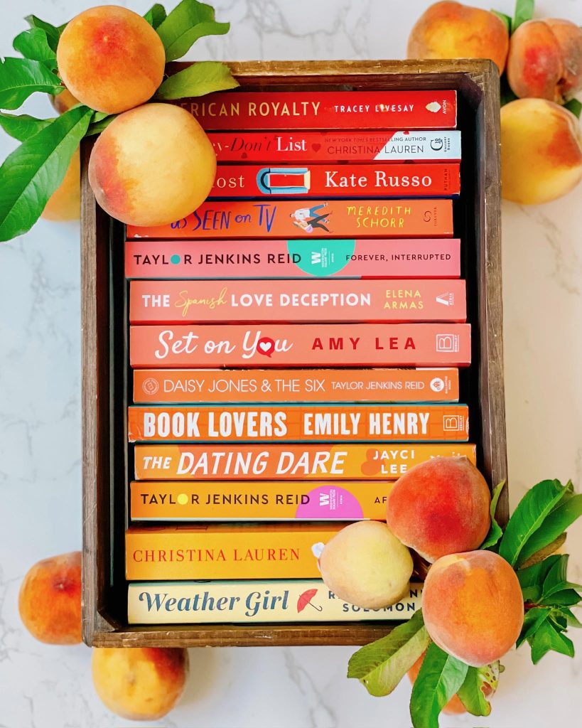 red and orange themed books in a wood basket surrounded by peaches and leaves on the edges.