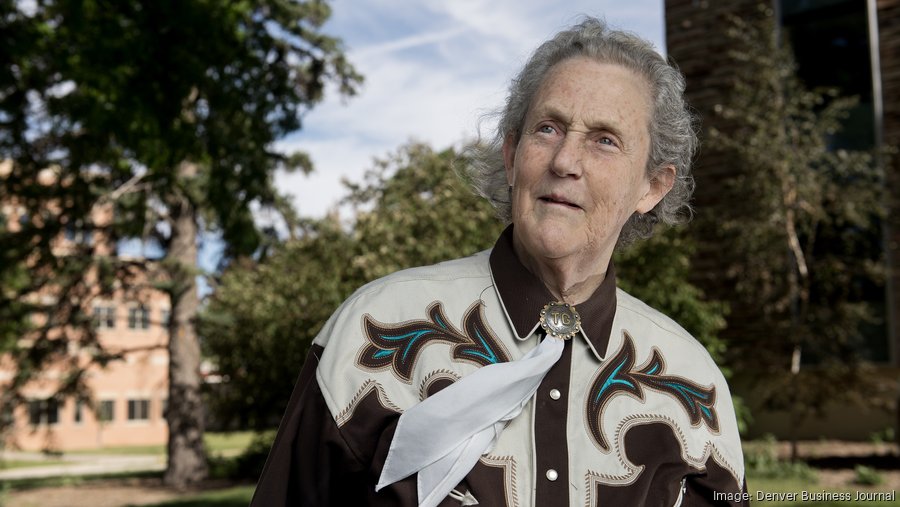 Author Temple Grandin stands outside and smiles. She looks to the right and wears a white and brown western blouse.