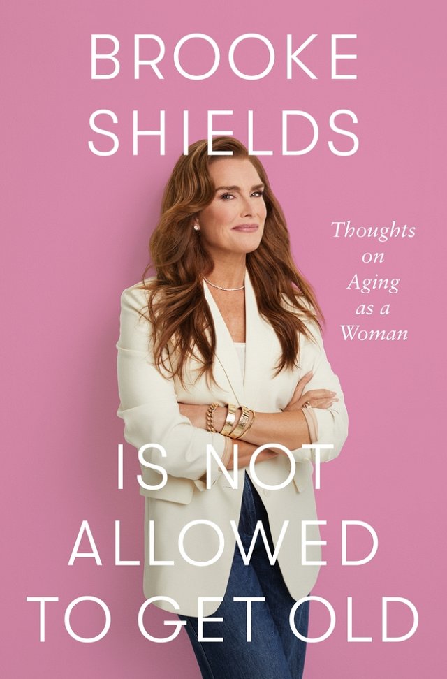 Brooke Shields in a white blazer with a pink background.