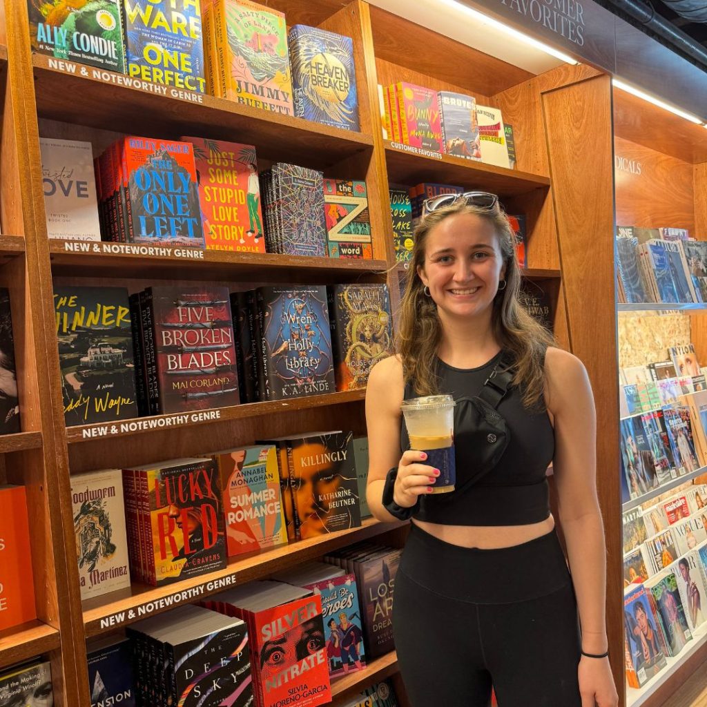 Kerryann holding a coffee and standing in front of a bookshelf in a book store.