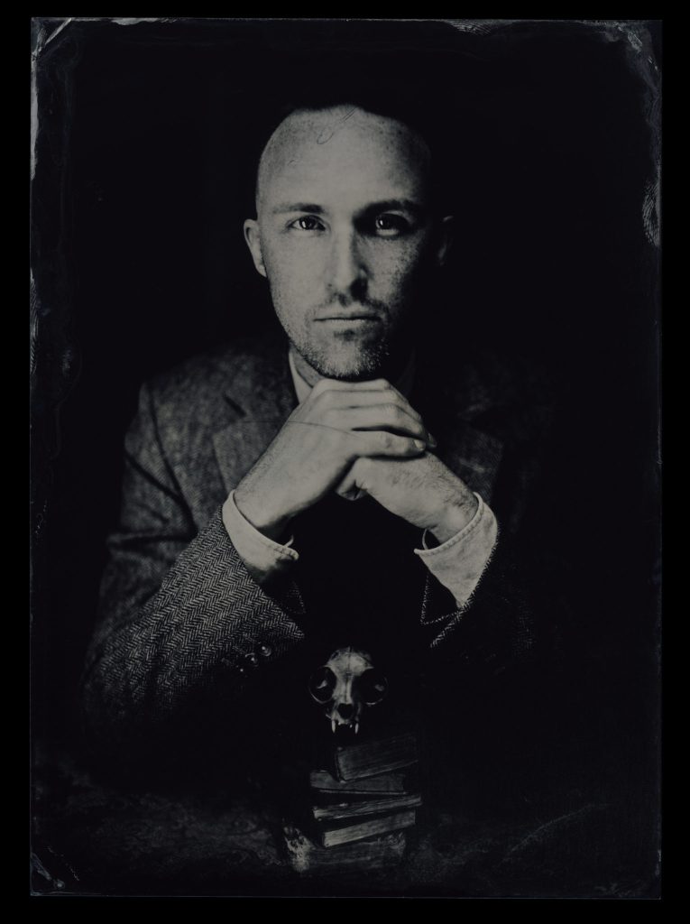Portrait of Per Faxneld. He is sitting in a tweed suit, looking at the camera with his hands in front of him.