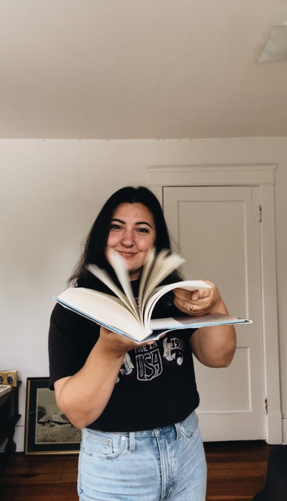Kenzie G. flipping the pages of a book while facing the viewer.