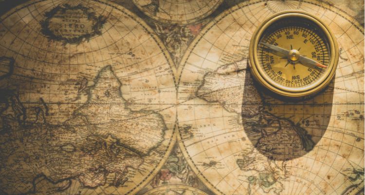 An antique map of the world and a gold-colored magnetic compass.