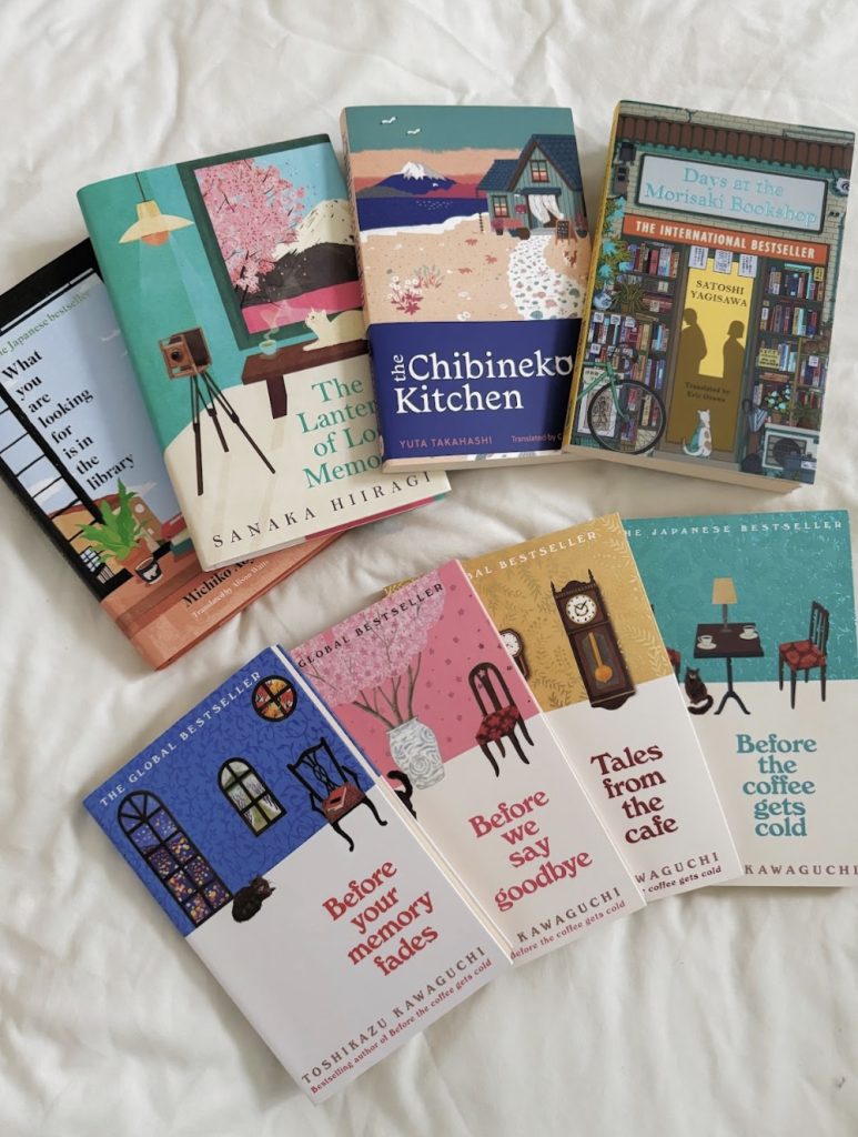 Image of a spread of eight books on a sheet, split into two rows of four. The row on top from left to right has: What You Are Looking For Is In The Library by Michiko Aoyama, The Lantern Of Lost Memories by Sanaka Hiiragi, The Chibineko Kitchen by Yuta Takahashi, and Days at the Morisaki Bookshop by Satoshi Yagisawa. The bottom row from left to right has Before Your Memory Fades, Before We Say Goodnye. Takes From The Cake, and Before The Coffee Gets Cold, all by Toshikazu Kawaguchi.
