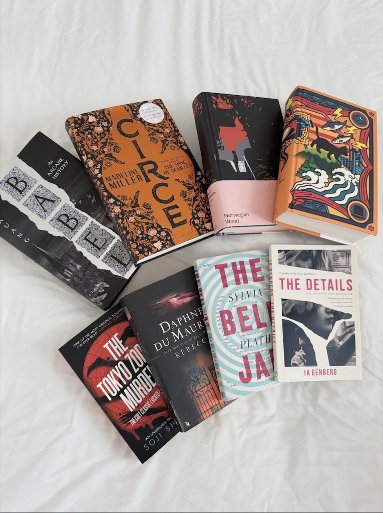 A spread of eight books on a sheet split into two rows of four. The top row from left to right has Babel by R.F. Kuang, Circe by Madeline Miller, Norwegian Wood by Haruki Murakami, and Kafka on the Shore also by Murakami.
