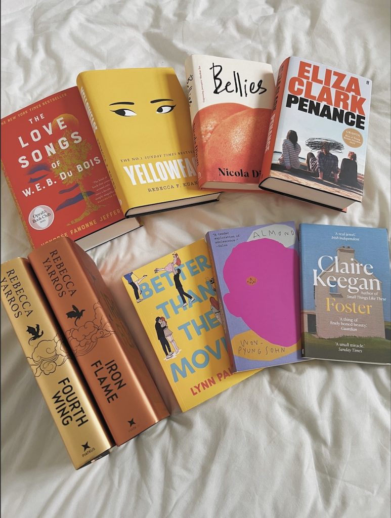 Spread of 9 books on a sheet. The top row of books from left to right is The Love Songs of W.E.B. Du Bois by Honorée Fanonne Jeffers, Yellowface by R.F. Kuang, Bellies by Nicola Dinan, and Penance by Eliza Clark. The bottom row has five books, the first two show only their spines while the rest show their covers. From left to right the books are Fourth Wing and Iron Flame by Rebecca Yarros, Better Than the Movies by Lynn Painter, Almond by Sohn Won-pyung, and Foster by Claire Keegan.