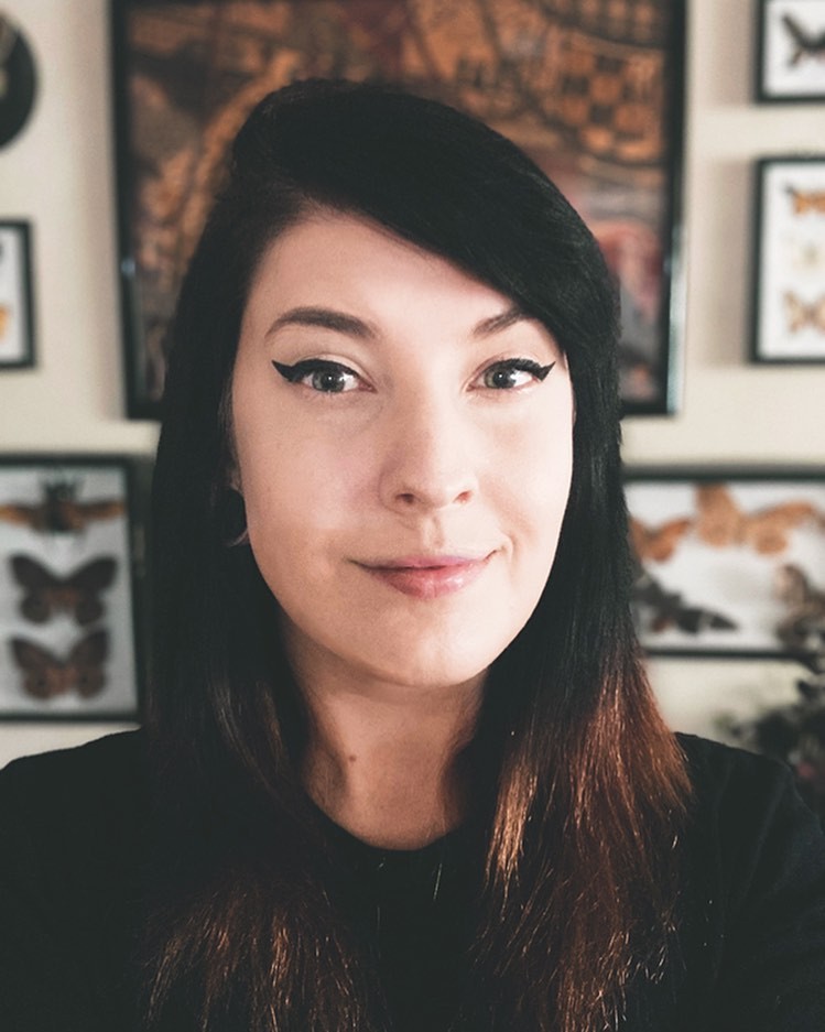 Head shot of Pamela Hoogeboom. She is standing in front of a wall with multiple frames of butterflies.