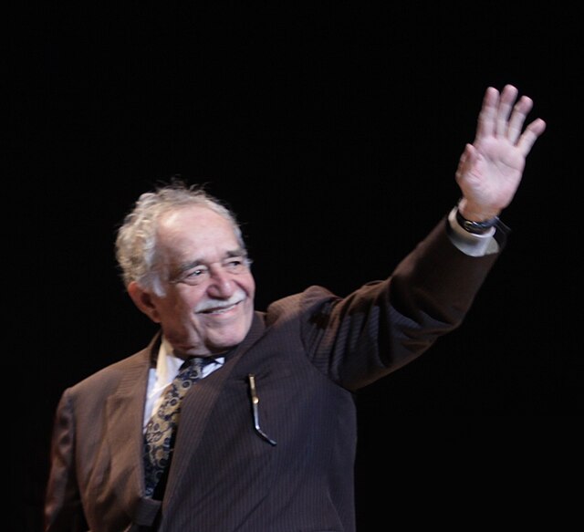 A photo of Gabriel Garcia Marquez on stage smiling and waving dressed in a suit.