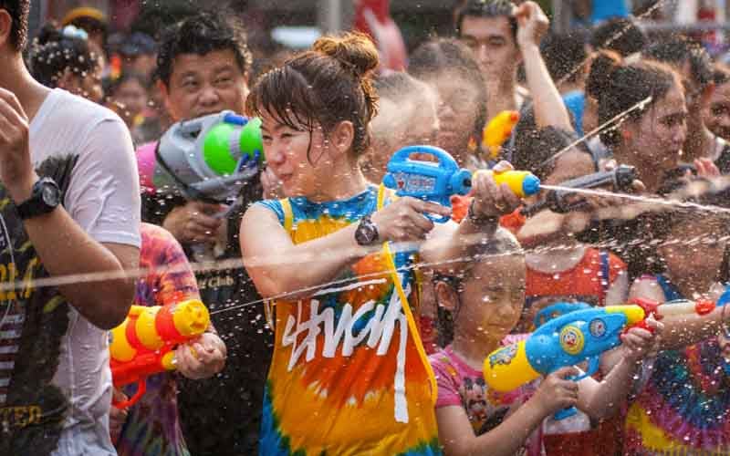 People joyfully splash water using water guns, celebrating the Thai New Year with a massive street water fight