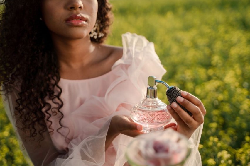 A woman sitting outside in a pink frilly dress with a bottle of perfume.