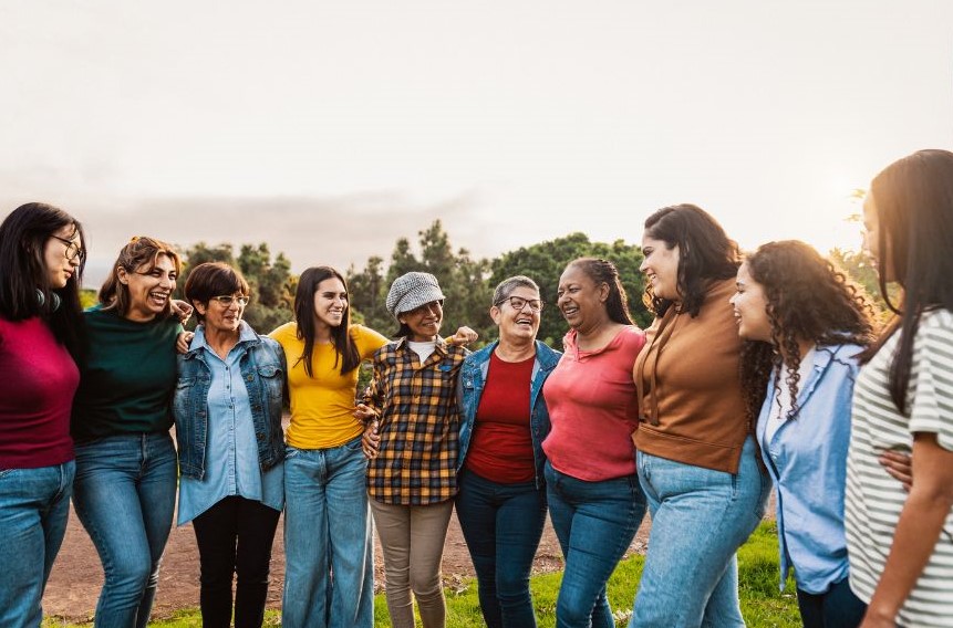 Ten women with their arms around each other and laughing and smiling.