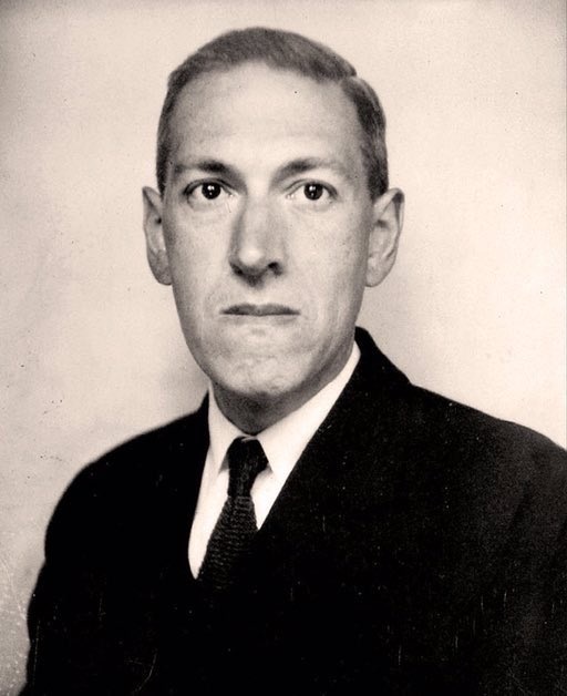 In black and white, H.P. Lovecraft wears a black suit and tie in front of a pale background.