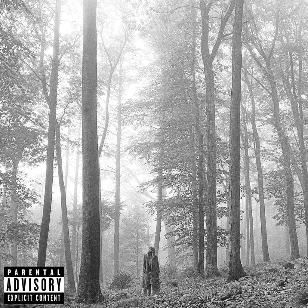 The album cover for folklore by Taylor Swift. From far away, Taylor Swift is depicted in black and white, standing among tall trees in a forest. In the bottom left corner is the "Explicit Content" advisory sticker.