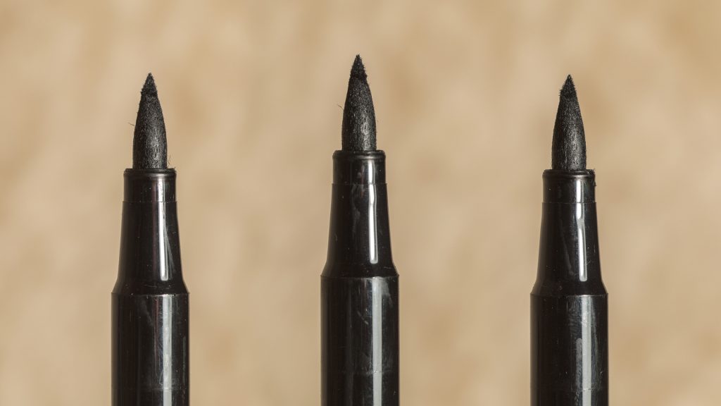 A blurred brown background. Three black markers missing their lids.