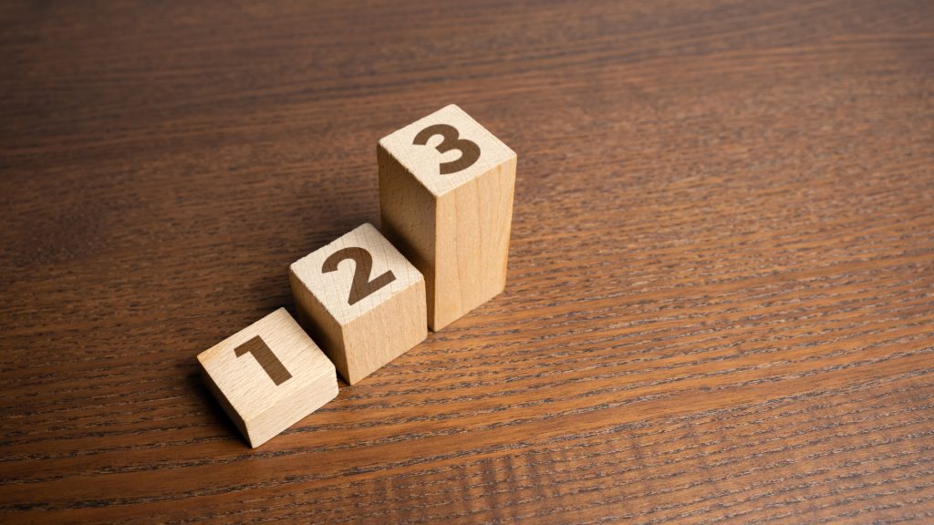 A wooden tabletop. Three graduated cubes with the numbers one, two, and three carved on them.