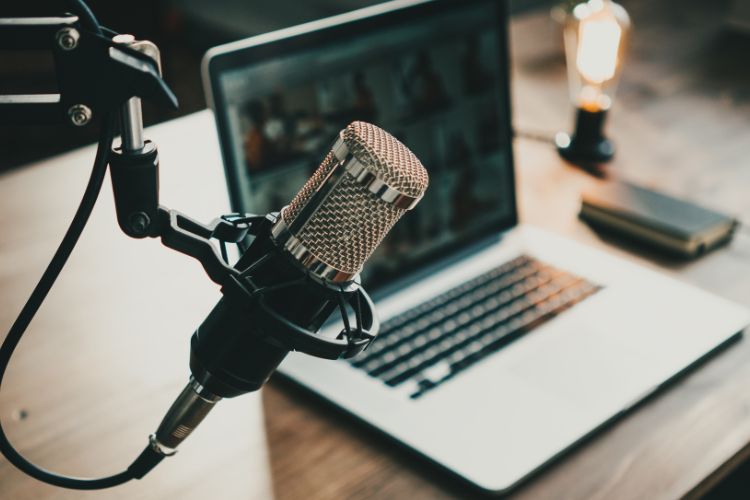 A microphone emerging from the left and a laptop on a wooden desk in the background.