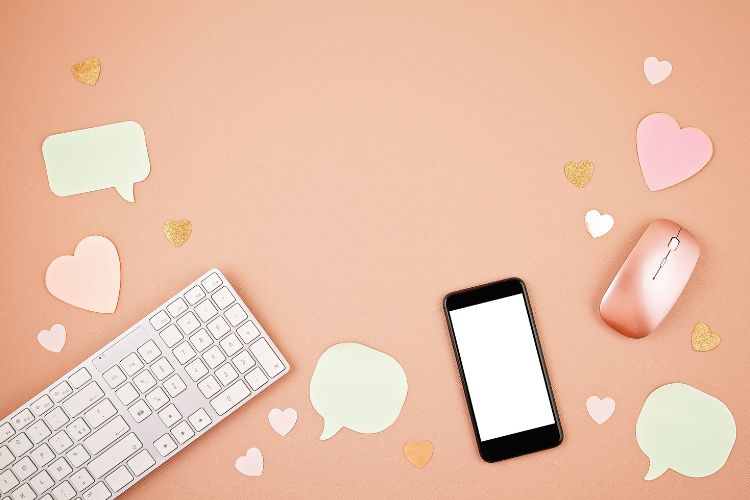 A keyboard, mouse, and phone and cut outs of comment bubbles and hearts against a pink background.