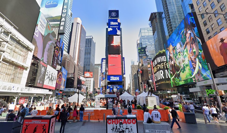 A crowded urban city street with dozens of pedestrians; large electronic billboards advertising various products and stage shows crowd the sides of buildings.