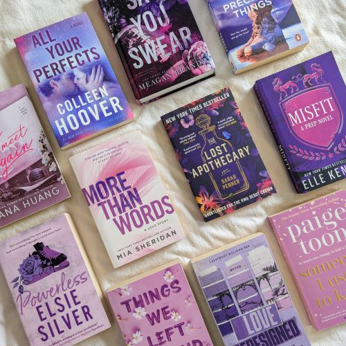 lottie-image-4 Eleven books oriented towards the top left corner with book covers varying in purple shades on top of a cream colored sheet.