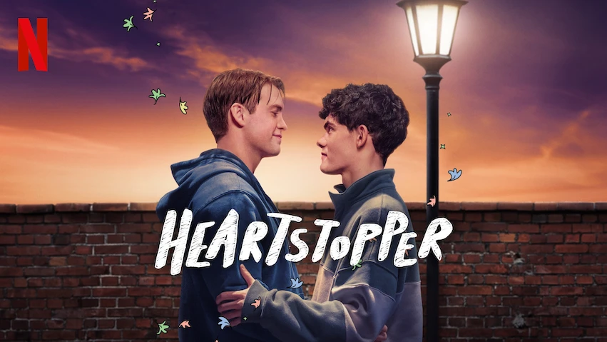 Promotional image for Netflix's 'Heartstopper,' featuring Nick and Charlie standing close together under a streetlamp at sunset, conveying romance and warmth in a heartfelt LGBTQ+ coming-of-age story.