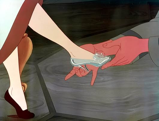 Two hands hold a woman's foot as it is placed into a sparkling glass slipper.