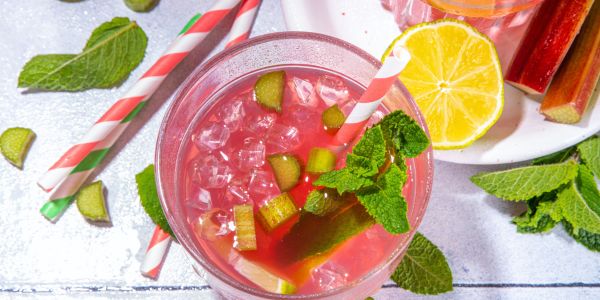 Top-view image of a bright pink drink with a pink and white swirl straw, small ice cubes, chunks of rhubarb, and a mint garmish.