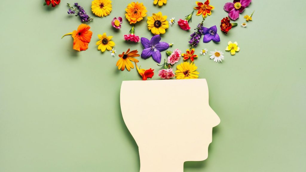 A side profile of a head with flowers coming out of the top against a sage green background.