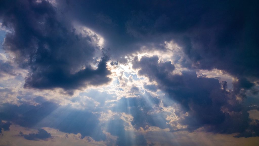 Rays of sunlight shine through a layer of thick, dark clouds.