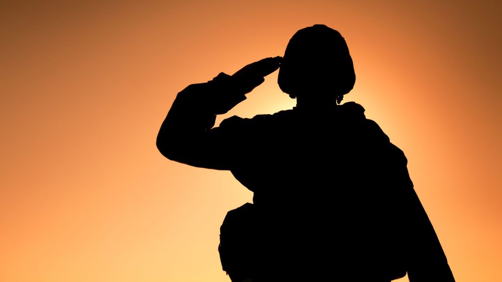 A soldier's silhouette saluting in front of a golden, sunny backdrop.