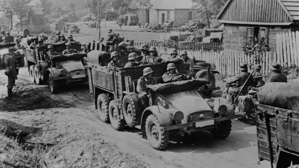 German soldiers in armored trucks drive down a dirt road to invade Poland at the beginning of World War II.
