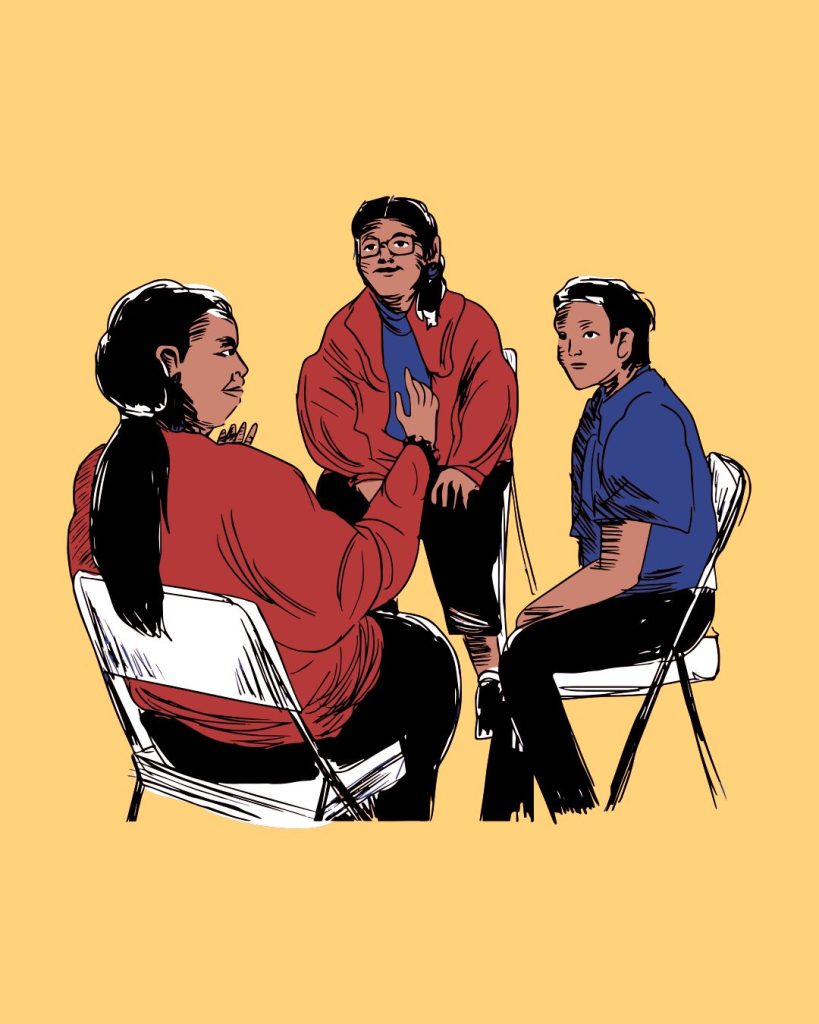3 Native Americans sit in folding chairs with blue shirts, black jeans (with 2 wearing red jackets in addition). Yellow background.