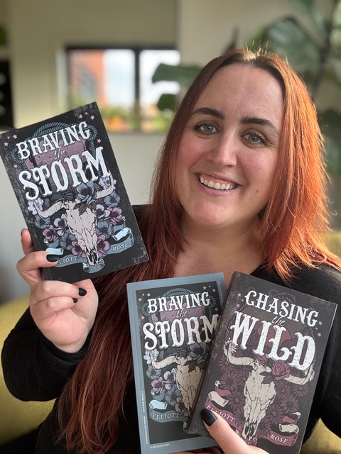 Cait holding Braving the Storm and Chasing the Wild by Elliot Rose.