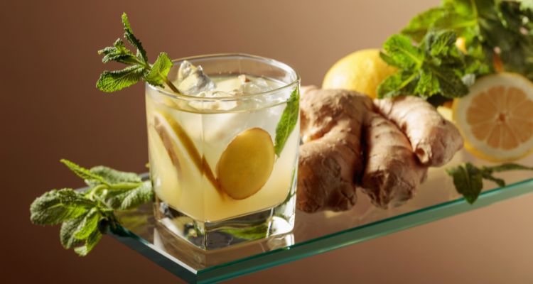 A cloudy yellow drink in a short square glass with lemon slices and mint and a shred of ginger.