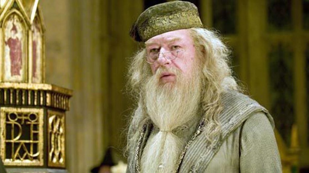 A still shot from the Harry Potter films of Albus Dumbledore, and older white man with long white hair and beard wearing long gray robes and semi-circular glasses