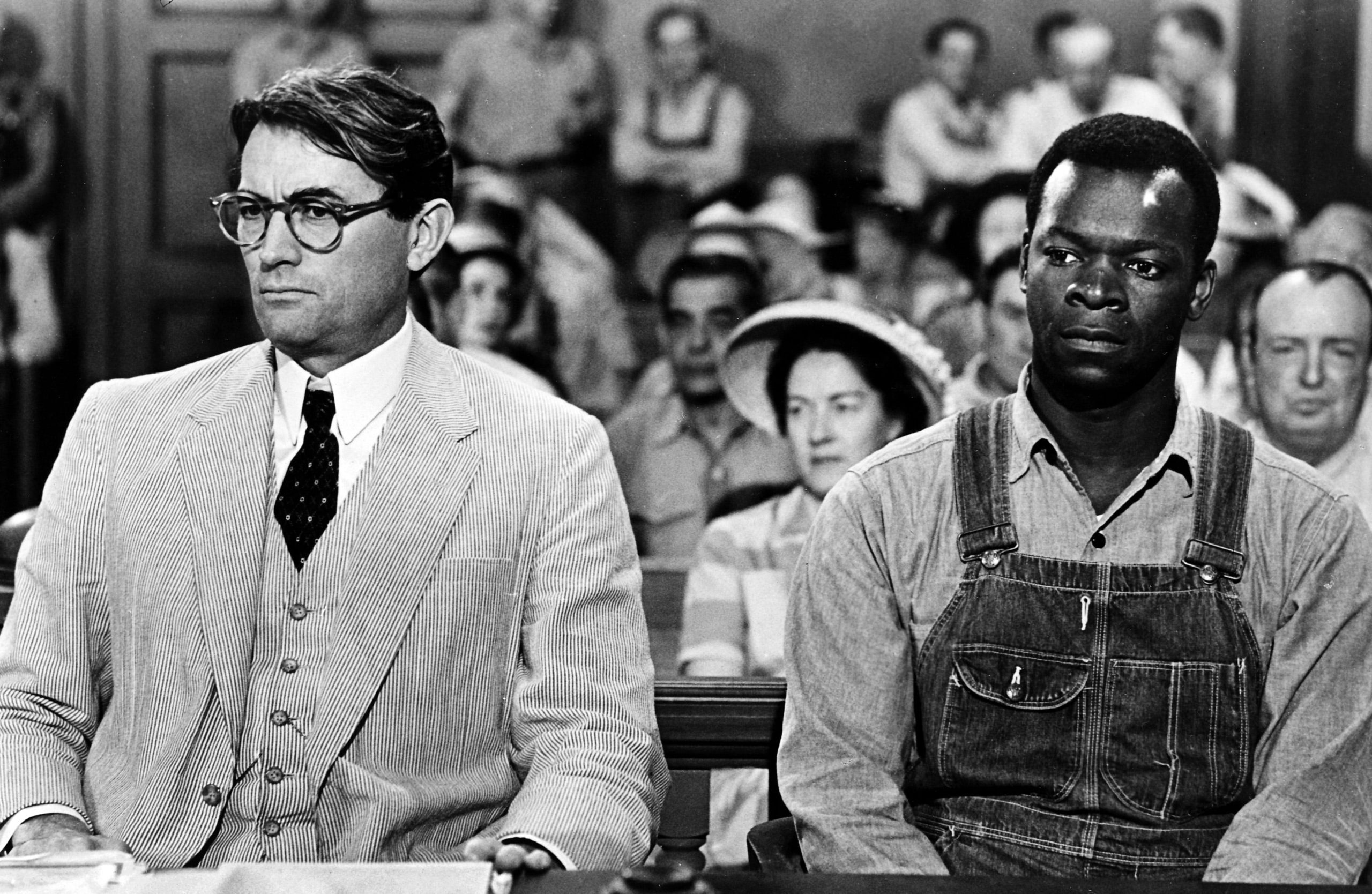 Black-and-white image from To Kill a Mockingbird film adaptation from Universal Pictures depicting a lawyer and his client sat in court.