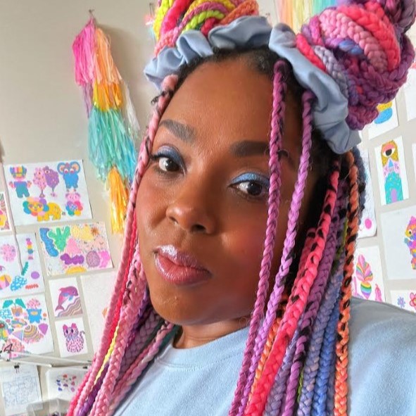 Amina Mucciolo, a slightly smiling brown-skinned person with long, colorful braids, some of which are tied into two buns on their head, and brown eyes, wearing bright blue eyeshadow and a blue shirt, standing in a room filled with colorful art covering the walls.